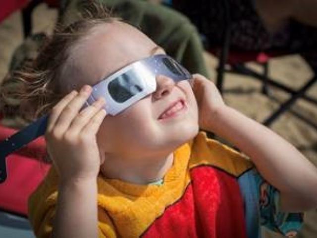 young girl viewing a total solar eclipse using specialized safety glasses. 