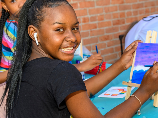 Photo of a young girl holding up a painting she made a Kids Arts Fest