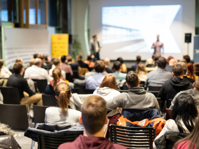 Photo of a classroom of people attending at class with a speaker and powerpoint presentation at the front