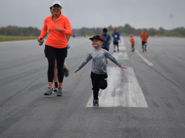 Photo of woman and kid running on the taxiway at the Schenectady County Airport during Run the Runway in 2023